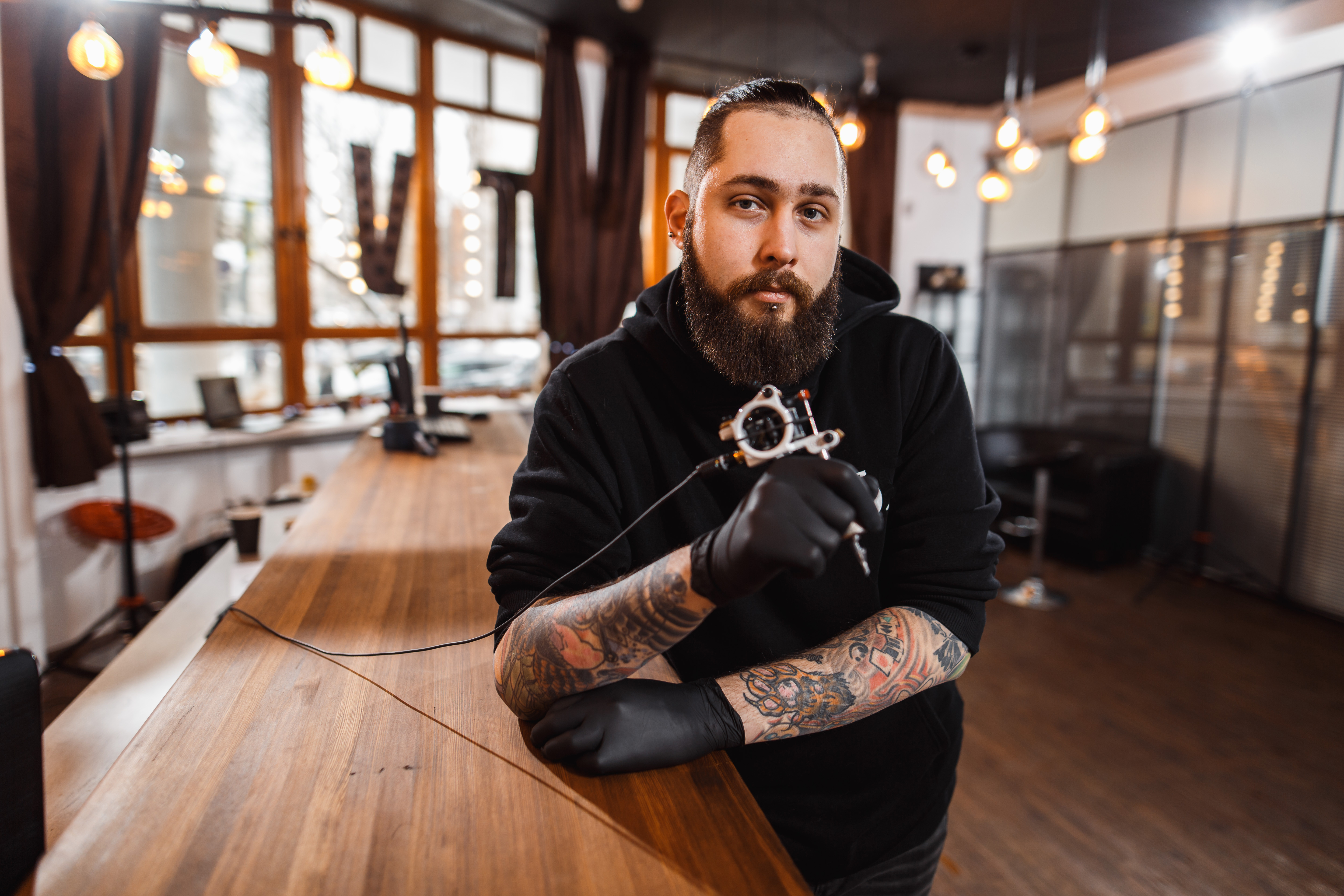 Portrait of professional creative tattoo master gloves in tattoo salon. Tattoo making process with machine gun.