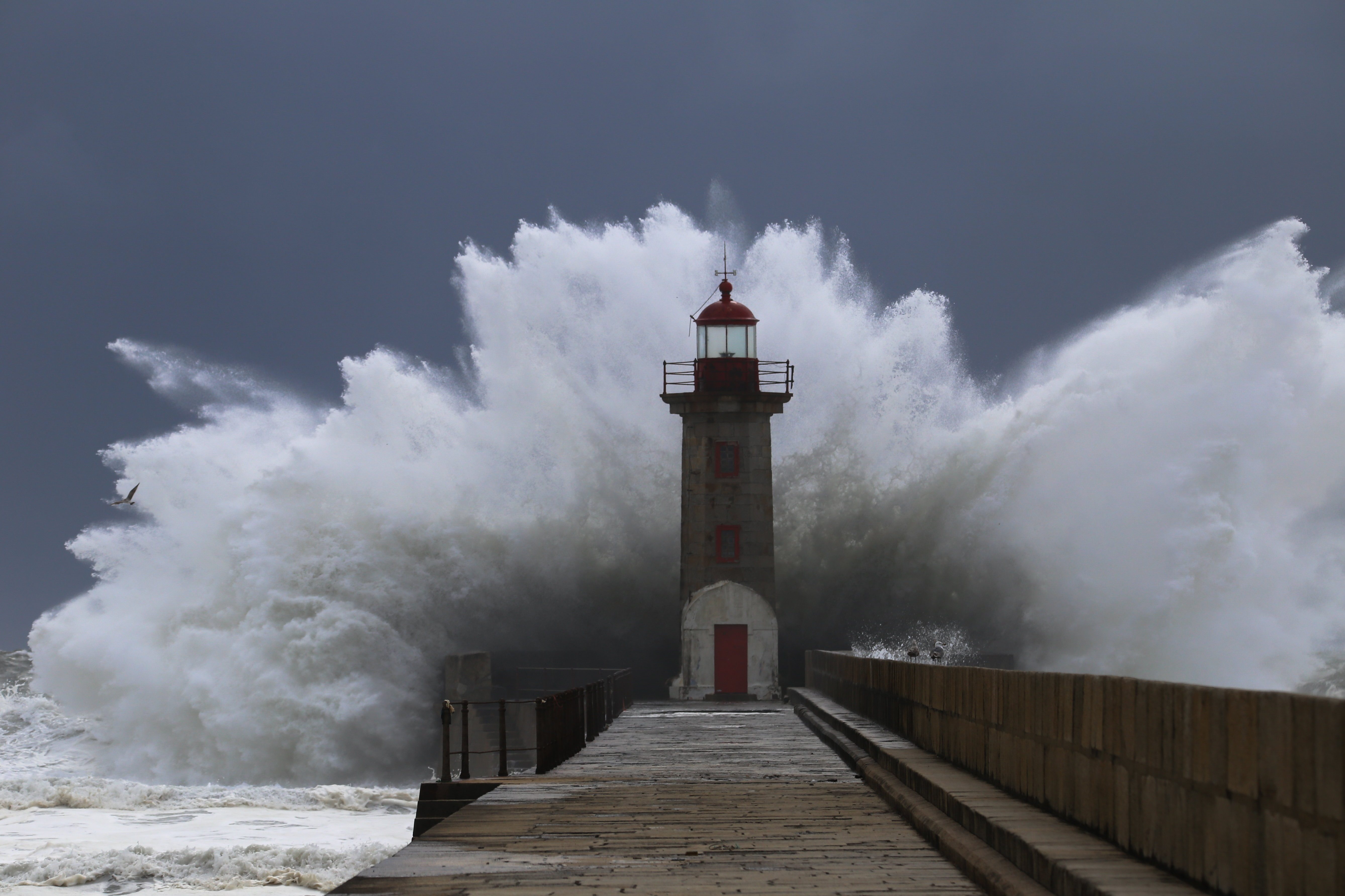 A big wave crashing behind a lighthouse.