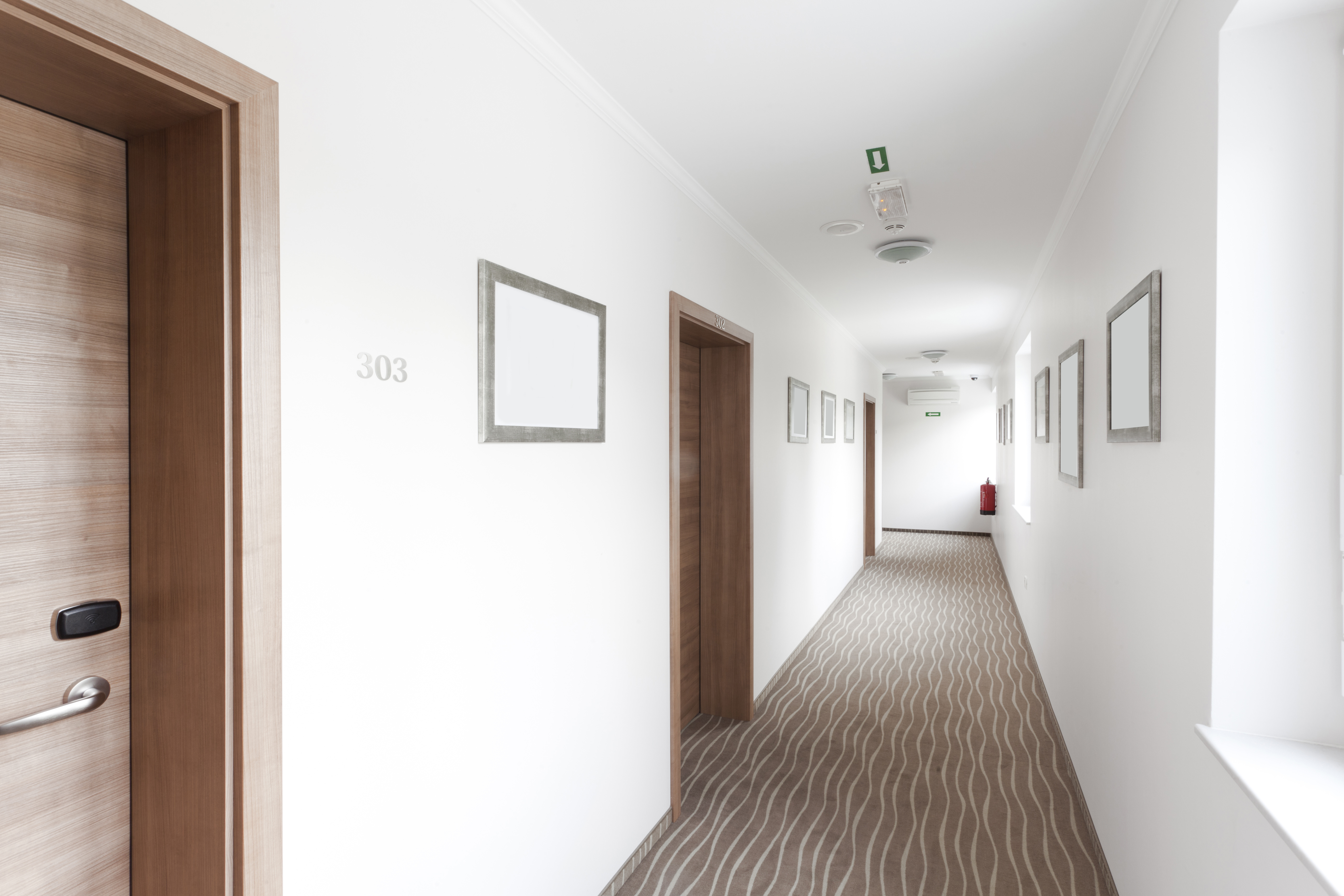 A corridor in a small hotel, with 2 doors to rooms and some pictures on the walls.
